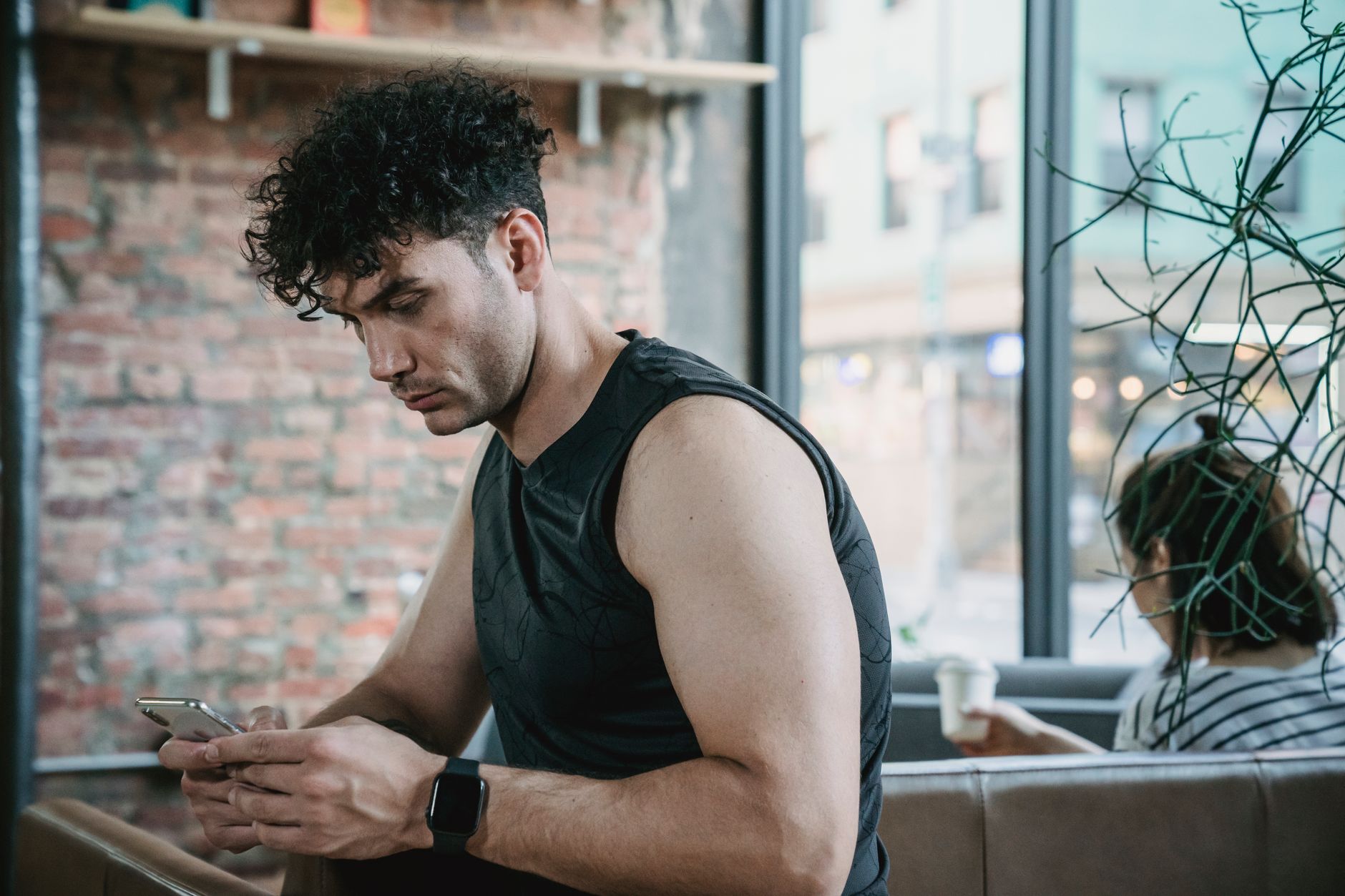 Homme en tenue de sport, assis dans un café, qui tape un message sur son téléphone